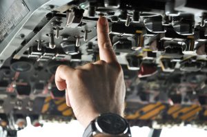 finger of a pilot pushing buttons in an airplane cockpit